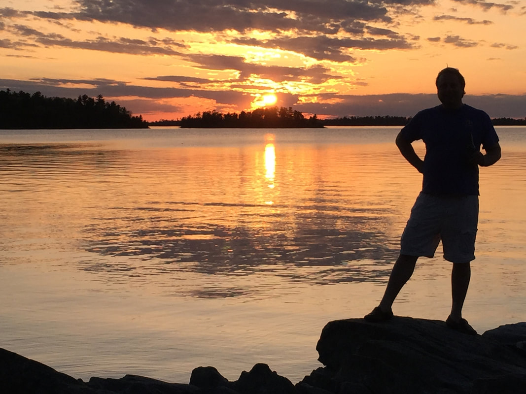 a man standing in front of a sunset over a body of water